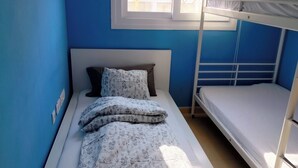 Une chambre avec un lit superposé, des murs bleus, une tête de lit blanche et une fenêtre située au-dessus du lit.