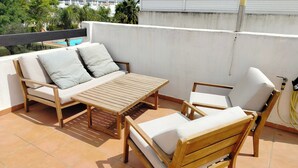 Une terrasse avec une table en bois, deux canapés, une chaise et une petite piscine.