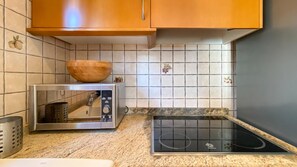 A kitchen with a microwave, an induction cooktop, and wooden cabinets. - Villa El Palmar 2 en Denia (Denia)