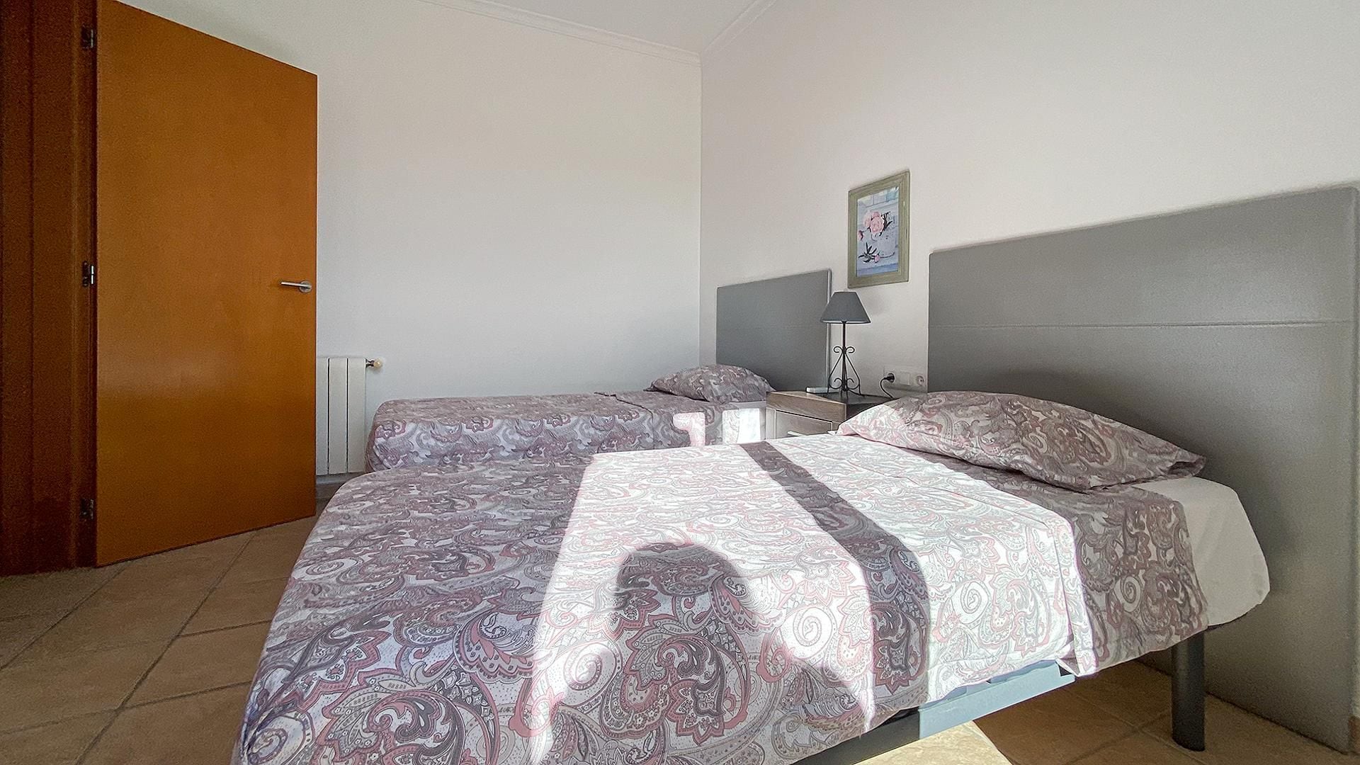 A bedroom with a bed, a nightstand, a lamp, a door, and a wall-mounted picture.