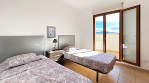 A hotel room with two beds, a nightstand, a lamp, and a sliding glass door leading to a balcony. - Villa El Palmar 2 en Denia (Denia)
