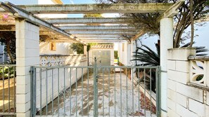 A gated entrance with a metal gate, a covered walkway, and a building with a door in the background. - Villa El Palmar 2 en Denia (Denia)