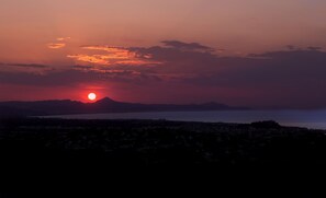 Un coucher de soleil sur une ville côtière, avec des montagnes en arrière-plan.