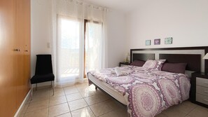 A bedroom with a bed, a chair, a nightstand, and a window with curtains. - Villa El Palmar 2 en Denia (Denia)
