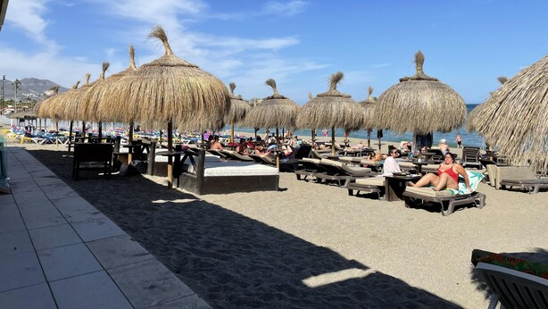 A beachside area with thatched umbrellas, lounge chairs, and a tiled walkway. - Newly Refurbished Luxury 3 Bed Duplex Apartment (Fuengirola)