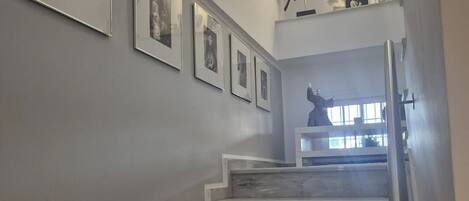 Una escalera de mármol con barandilla, que lleva a un rellano con una estatua y cuadros enmarcados en la pared.