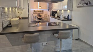 A modern kitchen with a central island, bar stools, a dining area with chairs, and a large window. - Newly Refurbished Luxury 3 Bed Duplex Apartment (Fuengirola)