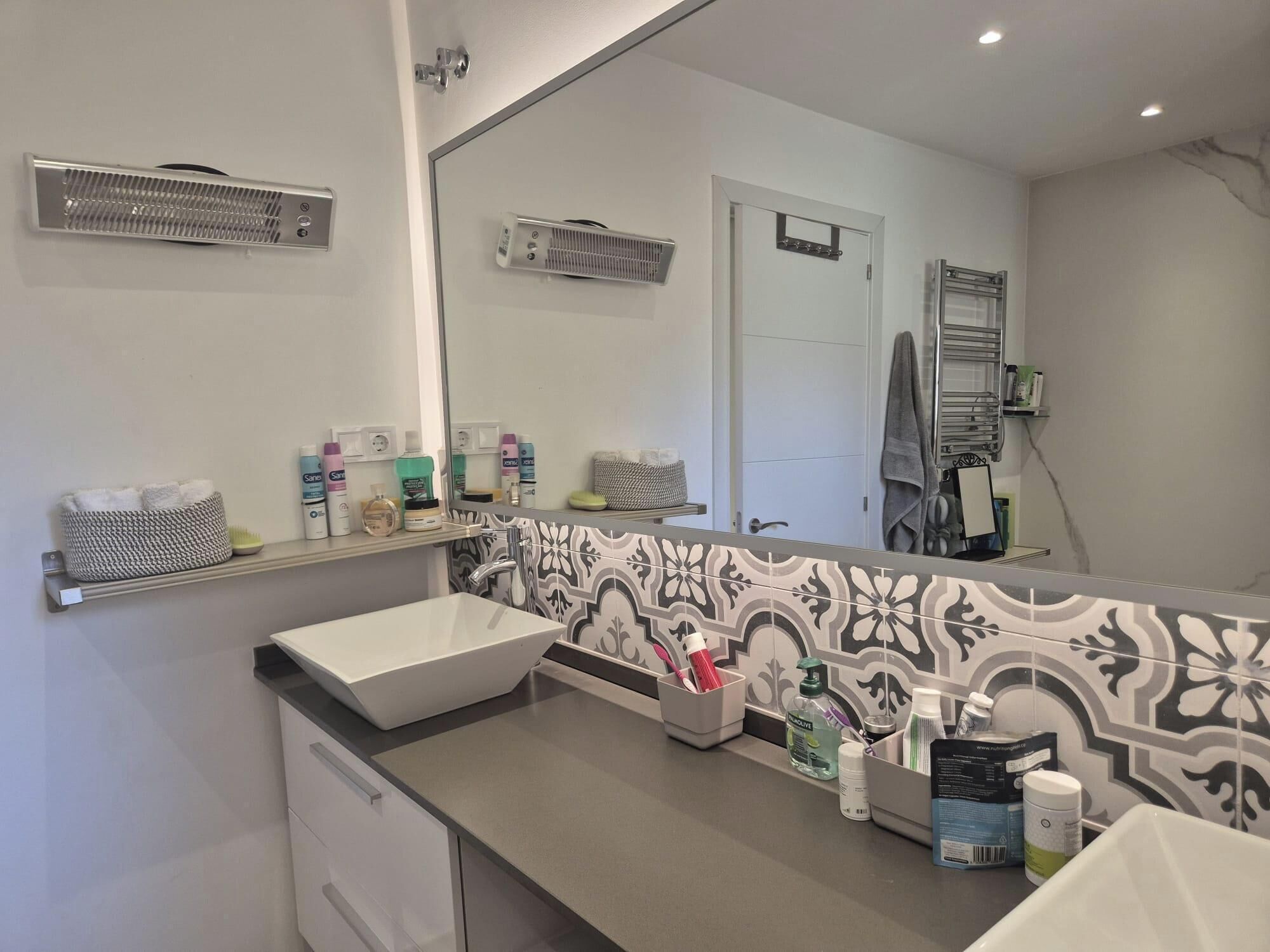 A modern bathroom with a large mirror, a white sink, and a tiled backsplash.