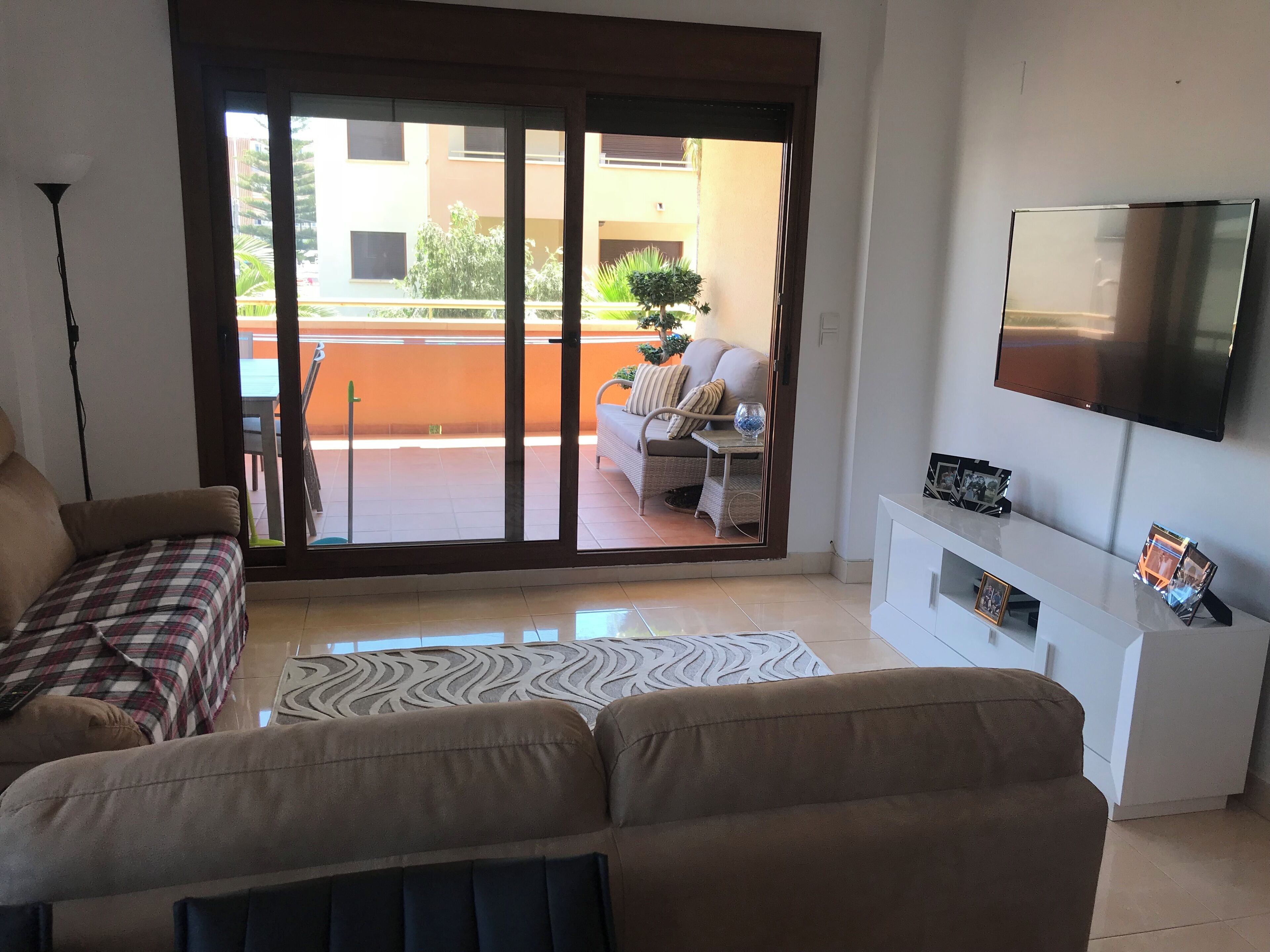 Un salon comprenant un canapé, un téléviseur fixé au mur et une porte-fenêtre coulissante donnant sur un espace extérieur avec un balcon.