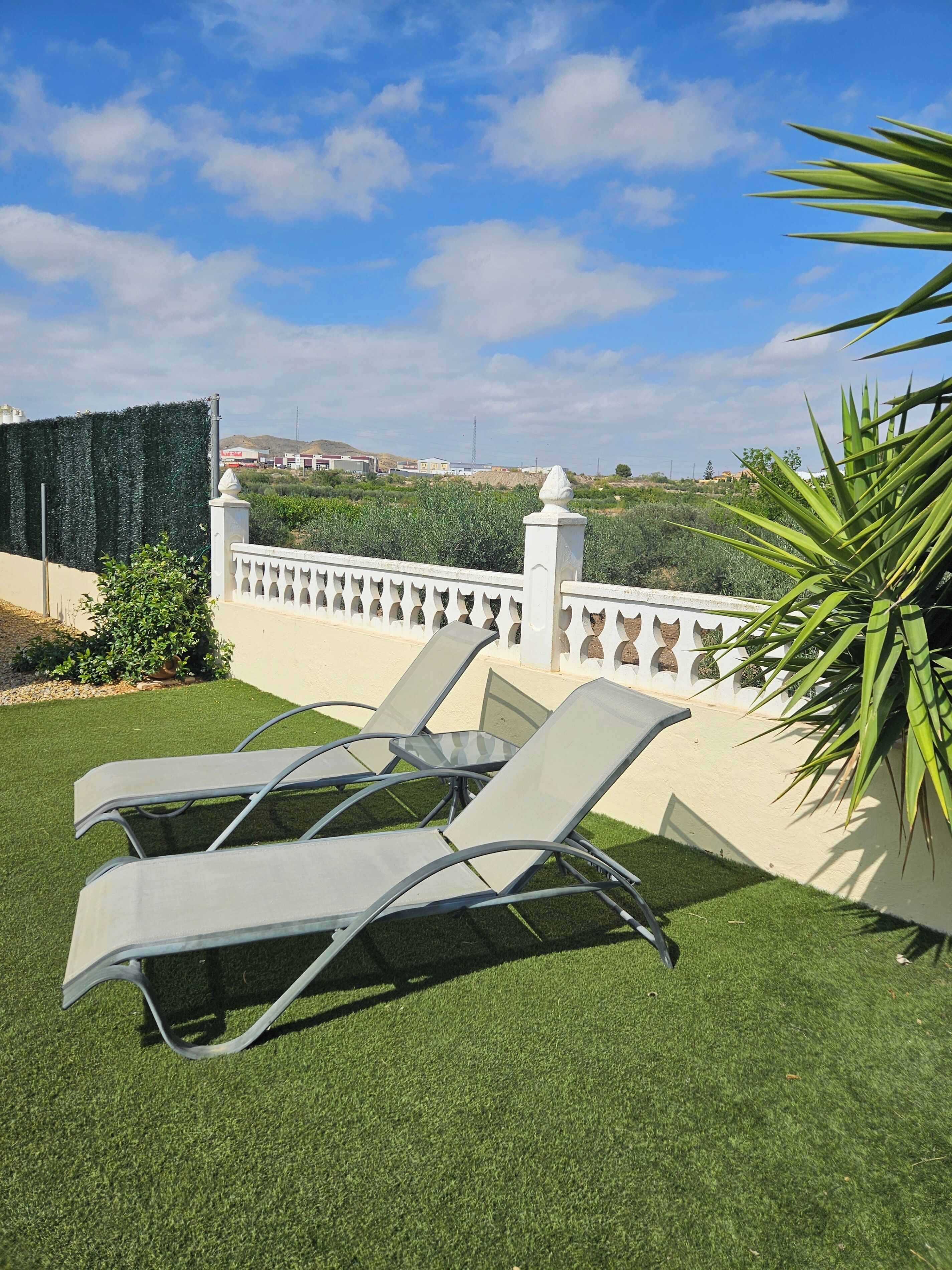 A patio with two lounge chairs and a white decorative fence.