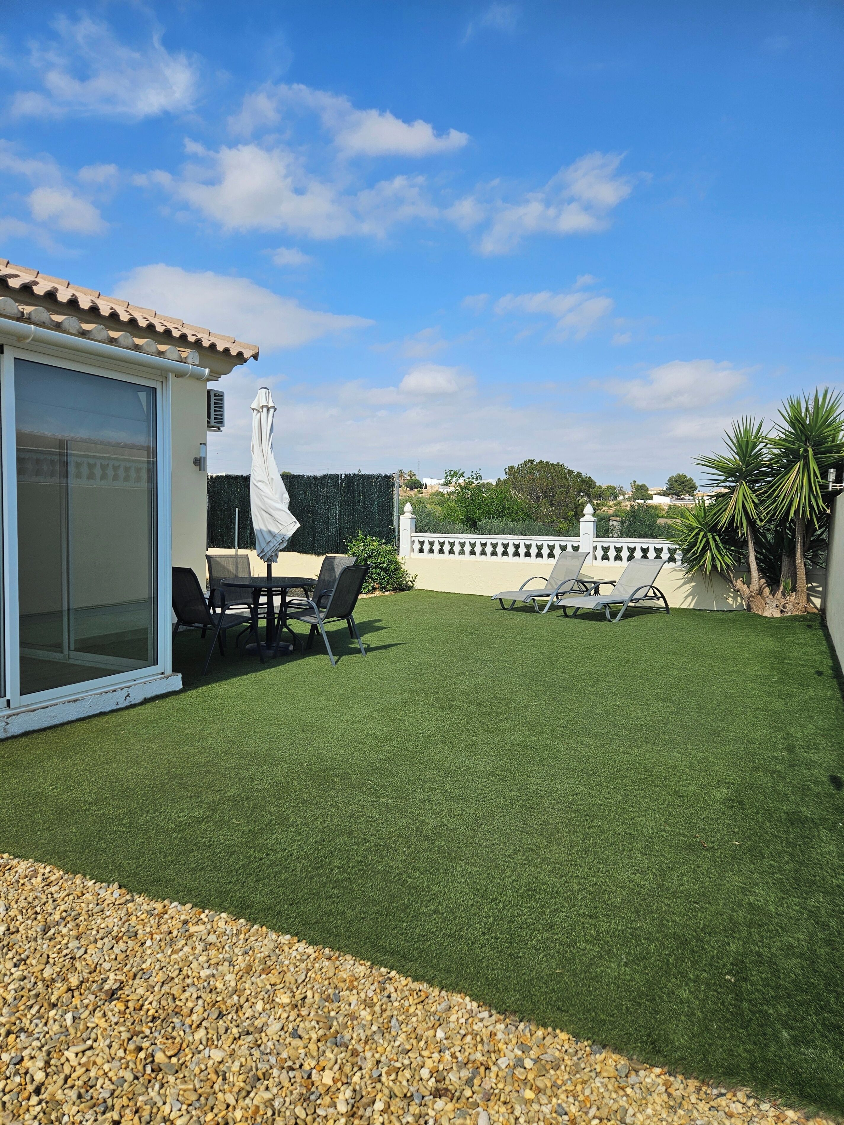 A patio with a table and chairs, a covered umbrella, and a white fence.
