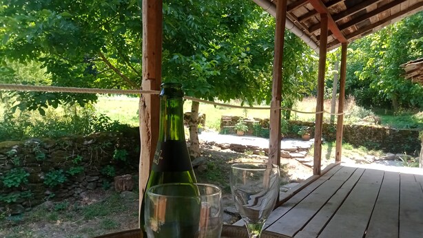 Een wijnfles en een glas op een houten tafel onder een houten pergola.