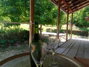 Una botella de vino y una copa sobre una mesa de madera, bajo una pérgola de madera.