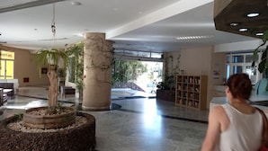 A spacious lobby with a central column, a reception desk, a bookshelf, and a large potted plant. - Cousy Holiday Apartment in Sunny Golf del Sur (San Miguel de Abona)