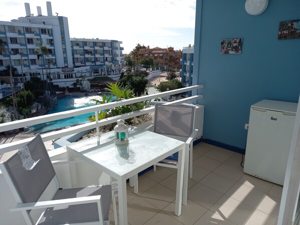 Een balkon met uitzicht op een zwembad, een tafel met een stoel, een koelkast en een muur met een schilderij.