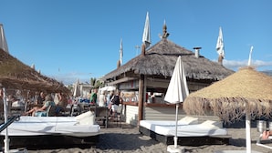 A beachside area with thatched-roof structures, lounge chairs, and a bar area. - Cousy Holiday Apartment in Sunny Golf del Sur (San Miguel de Abona)