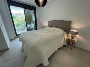 A bedroom with a large bed, a bedside lamp, and a view of the outdoors through a sliding door. - Modern Luxurious 3-bed Apartment in La Quinta Golf (Benahavis)