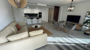 A modern living room with a sofa, coffee table, and dining area. - Modern Luxurious 3-bed Apartment in La Quinta Golf (Benahavis)