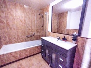 A bathroom with a bathtub, a sink, and a large mirror. - Charming 3 Bed Beach Apartment in Punta del Moral (Ayamonte)