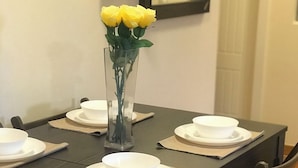 Una mesa de comedor dispuesta con platos y tazones blancos, y una jarra transparente con flores amarillas.