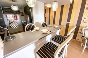 A dining area with a long table, striped chairs, and modern pendant lights.