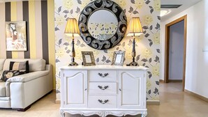 A living room with a white sofa, a white cabinet with decorative handles, two lamps, and a large mirror with a floral wallpaper background. - Apt Sleeps 4 With Pool Access (Torre-Pacheco)