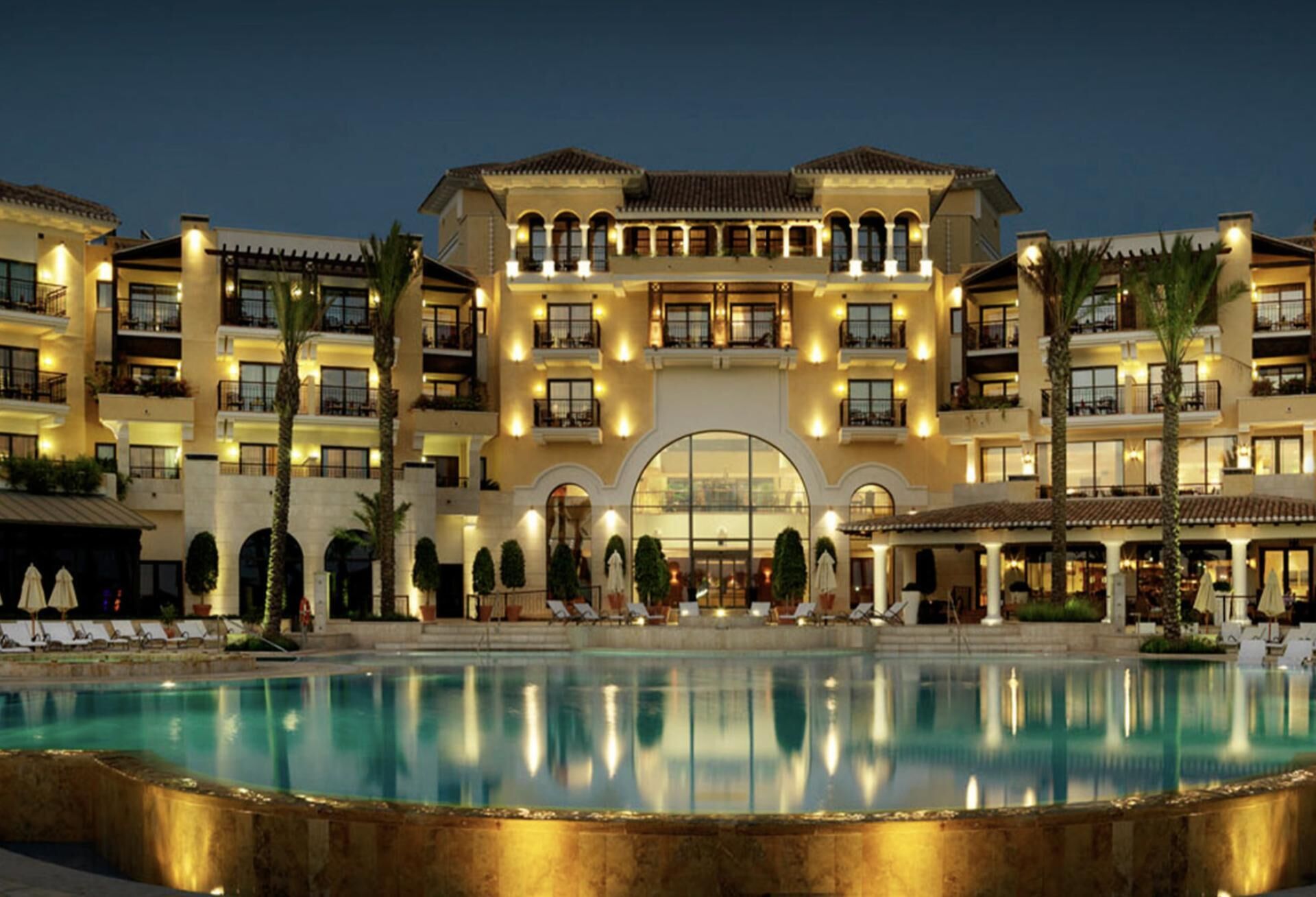 Um hotel com uma piscina grande, várias varandas e uma entrada central em arco.