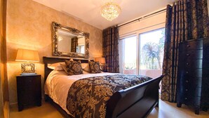 A bedroom with a large bed, a nightstand with a lamp, a dresser, a mirror, and a chandelier. - Apt Sleeps 4 With Pool Access (Torre-Pacheco)