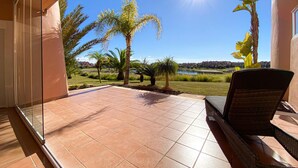A patio with a view of a lake and palm trees, a chair, and a tiled floor. - Apt Sleeps 4 With Pool Access (Torre-Pacheco)