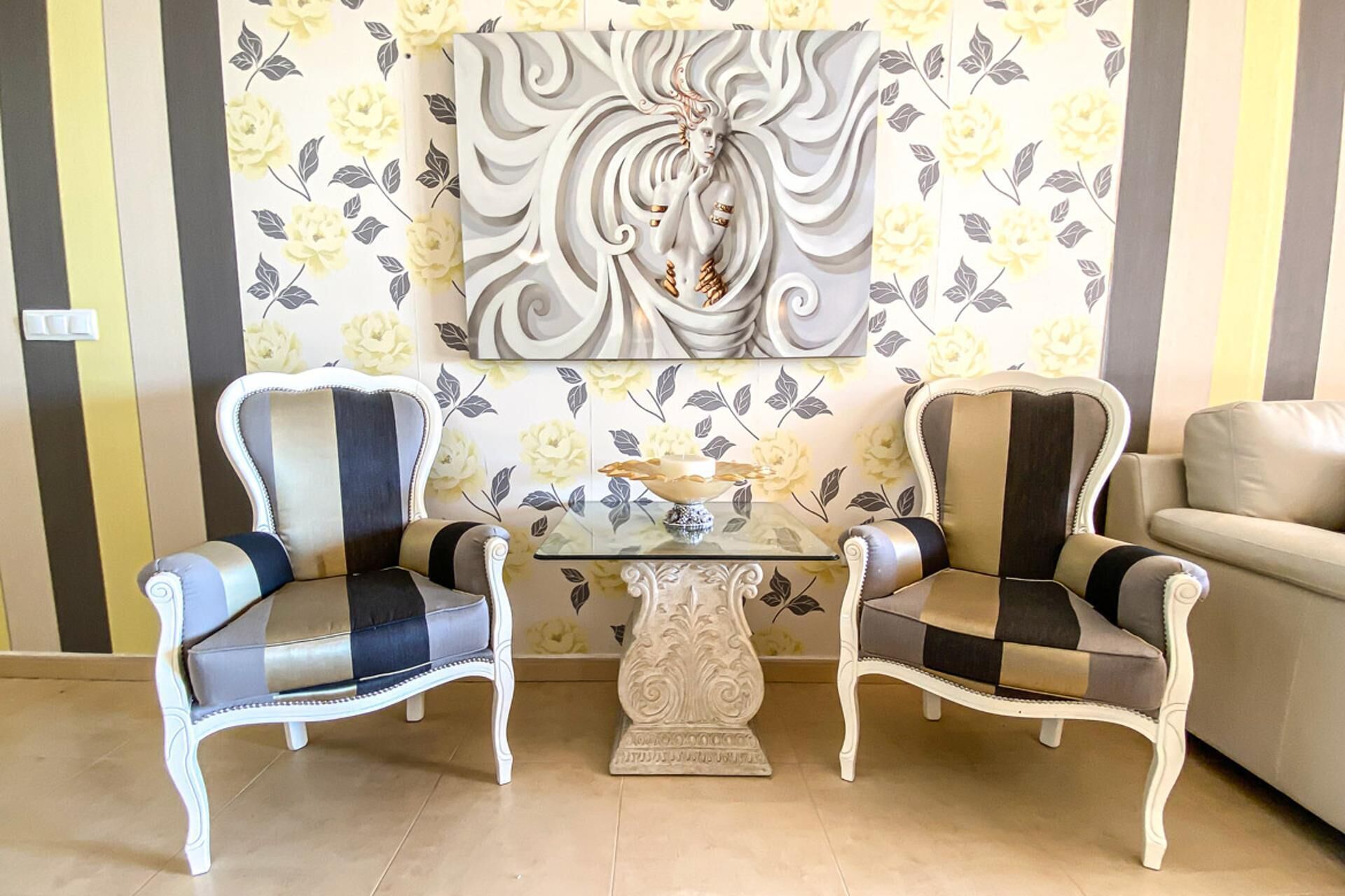Een kamer met twee fauteuils, een glazen salontafel en bloemenbehang.
