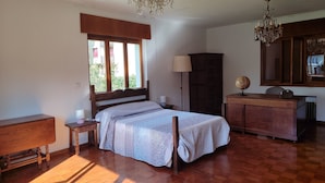 A bedroom with a wooden floor, a bed with patterned bedding, a dresser, a lamp, a globe, and a chandelier. - Charming 6-bed Chalet in Llanes (Llanes)