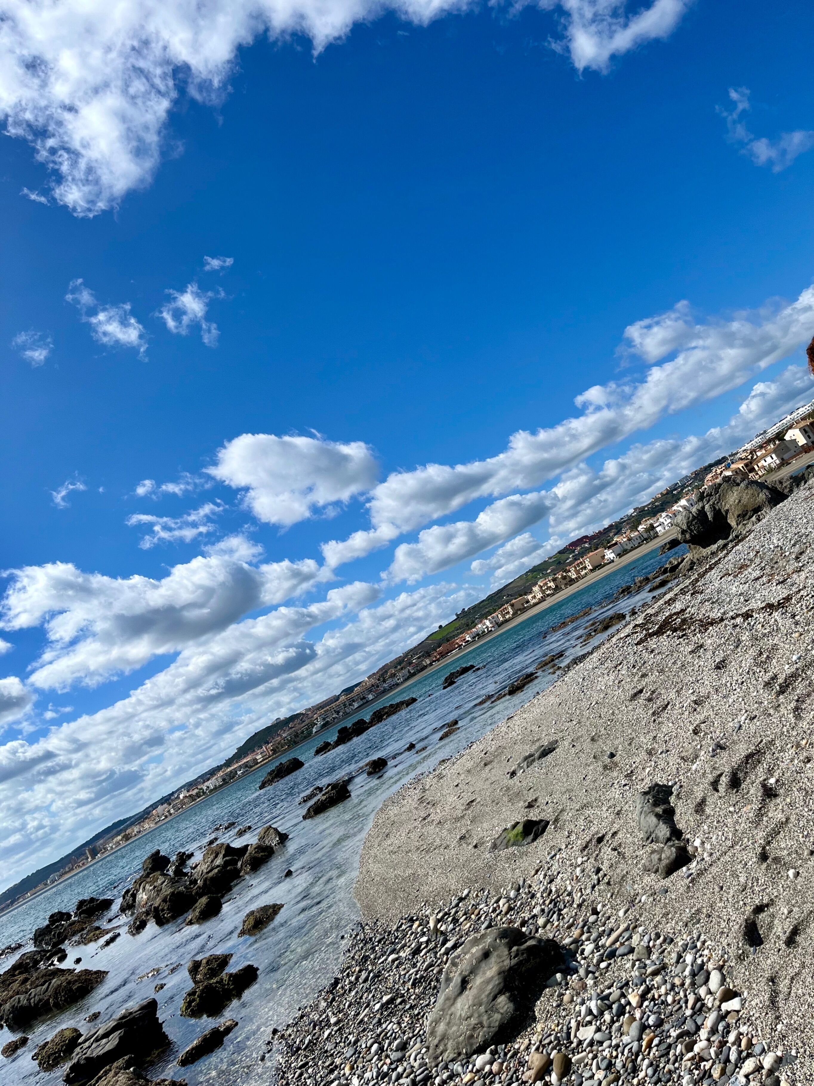 A coastal landscape with a rocky shoreline, clear blue sky, and distant buildings.