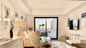 Ett modernt hotellrum med ett marmorgolv, en soffa, en fåtölj, en TV och en balkong med utsikt.