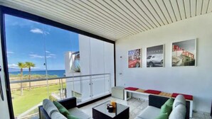 Ett modernt vardagsrum med en stor skjutdörr i glas som leder ut till en balkong med utsikt över en strand.