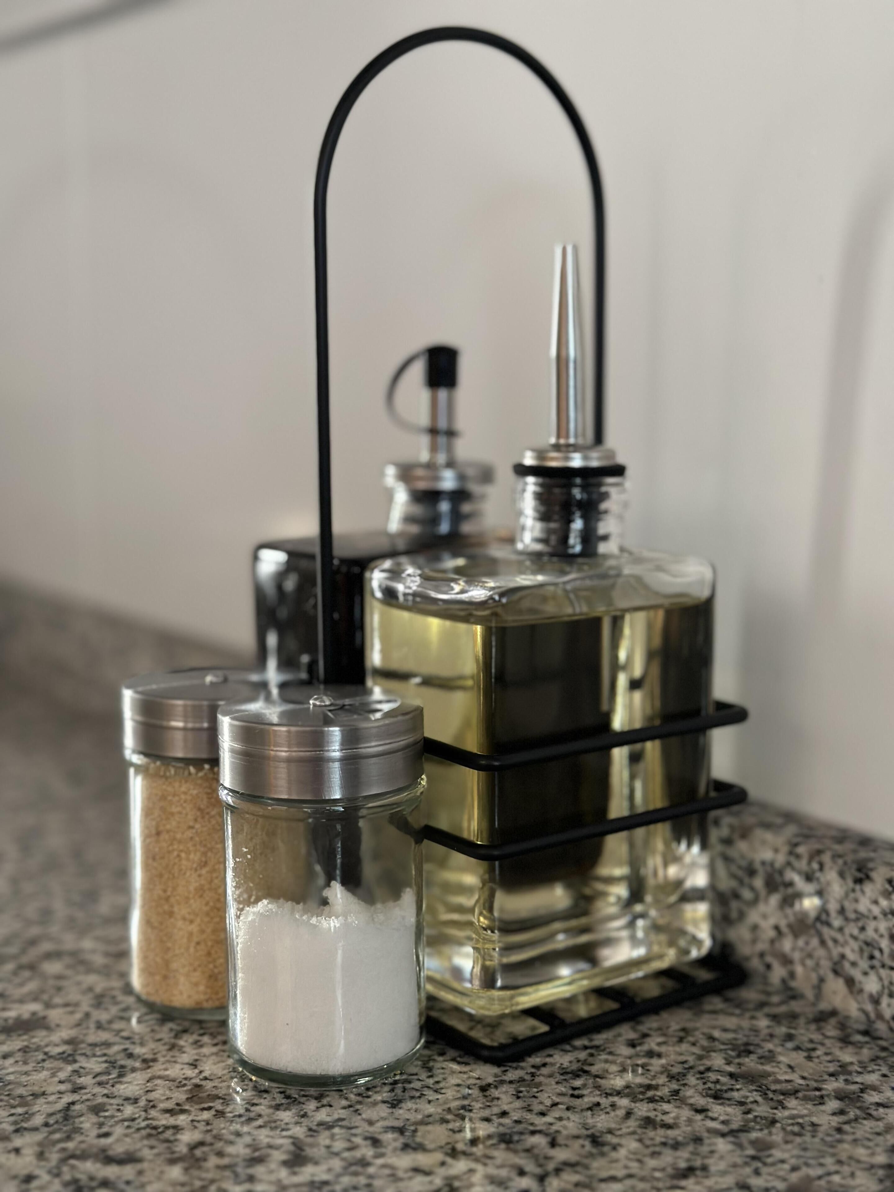 A kitchen counter with a spice rack holding two glass jars and a metal container with a black handle.