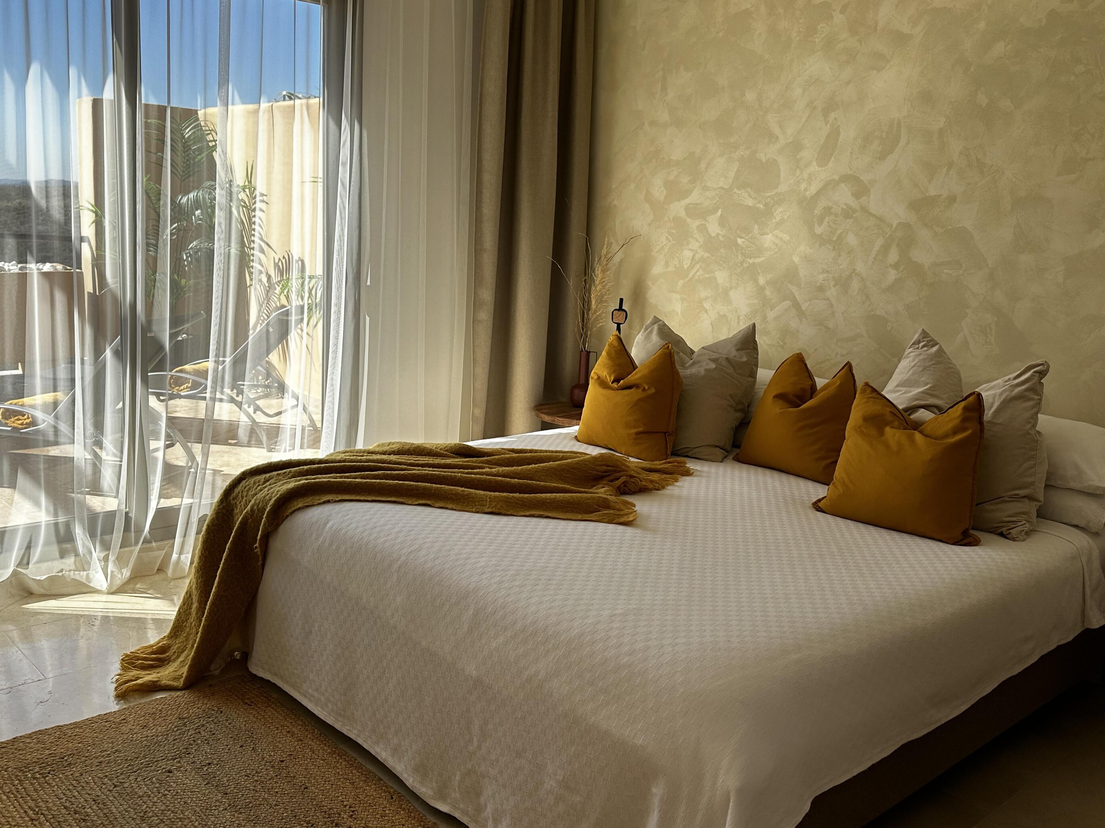 A bedroom with a large bed, a view of the outdoors, and a window with sheer curtains.