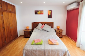 Quarto com guarda-roupa de madeira, uma cama com duas almofadas, duas mesas de cabeceira com luminárias e um ar condicionado.