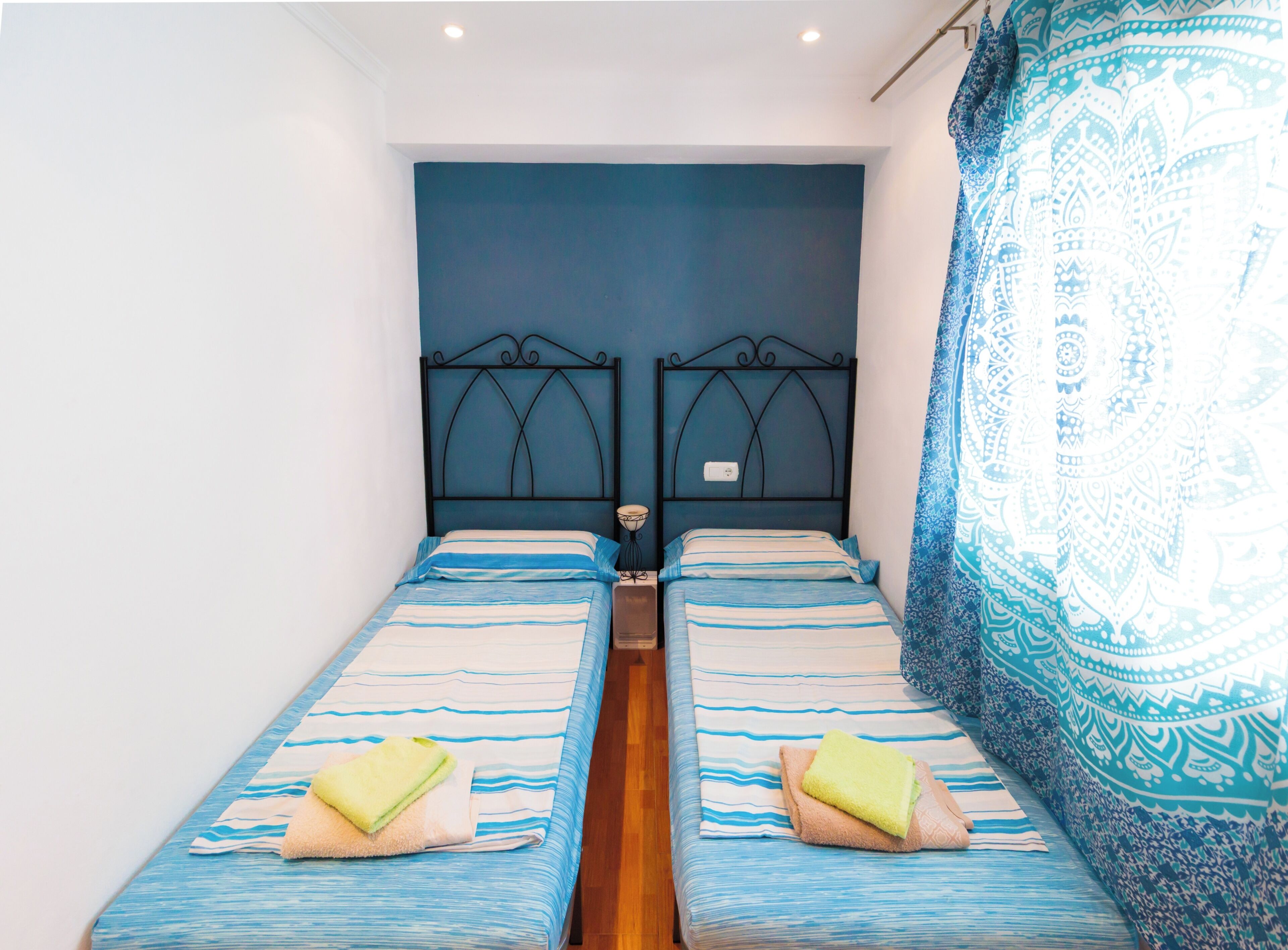 A room with two single beds, each with a headboard, a bedside table, and a lamp.