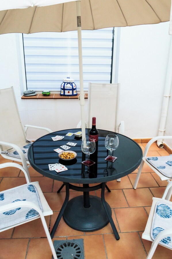 A round table with a black metal frame, surrounded by white chairs with blue patterns. On the table, there are playing cards, a bottle of wine, and two wine glasses. - Frigiliana 3-bed Apartment- Sleeps 8 (Frigiliana)