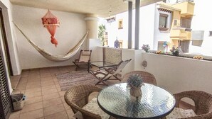 A balcony with wicker furniture, a hammock, and a glass table. - Lovely 2-bed Apartment in Costa Esuri (Ayamonte)