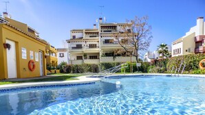 A swimming pool with clear blue water, surrounded by buildings with balconies and a well-maintained lawn. - Lovely 2-bed Apartment in Costa Esuri (Ayamonte)