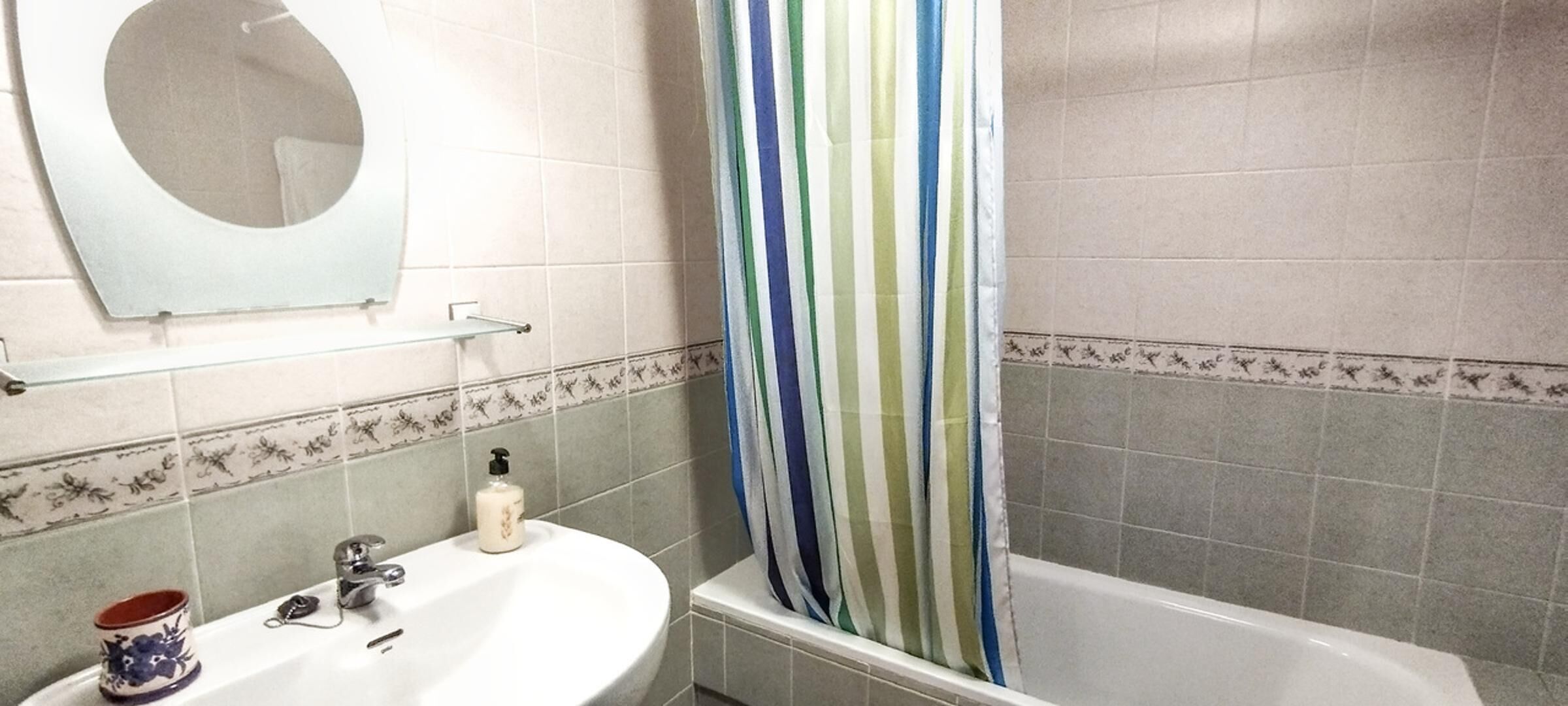 Un baño con lavamanos blanco, espejo, cortina de ducha a rayas y bañera.