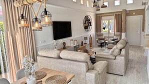A modern living room with a large flat-screen TV, beige sofas, a wooden dining table, and a unique rope chandelier. - Casa Bonita Sleeps 4 With Private Pool (Torre-Pacheco)