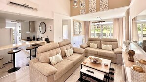A spacious living area with two sofas, a coffee table, and a dining table. There is a kitchen in the background with a clock and a window. - Casa Bonita Sleeps 4 With Private Pool (Torre-Pacheco)