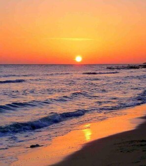 A sunset over the ocean with waves gently lapping at the shore.