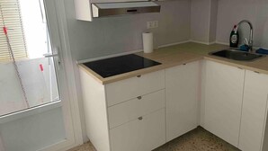 Una cucina compatta con mobili bianchi, un piano cottura a induzione nero, un lavello in acciaio inossidabile e una finestra con persiane.