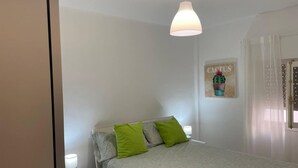 Una camera da letto con un letto, due cuscini verdi, un comodino con una lampada e un quadro appeso al muro.