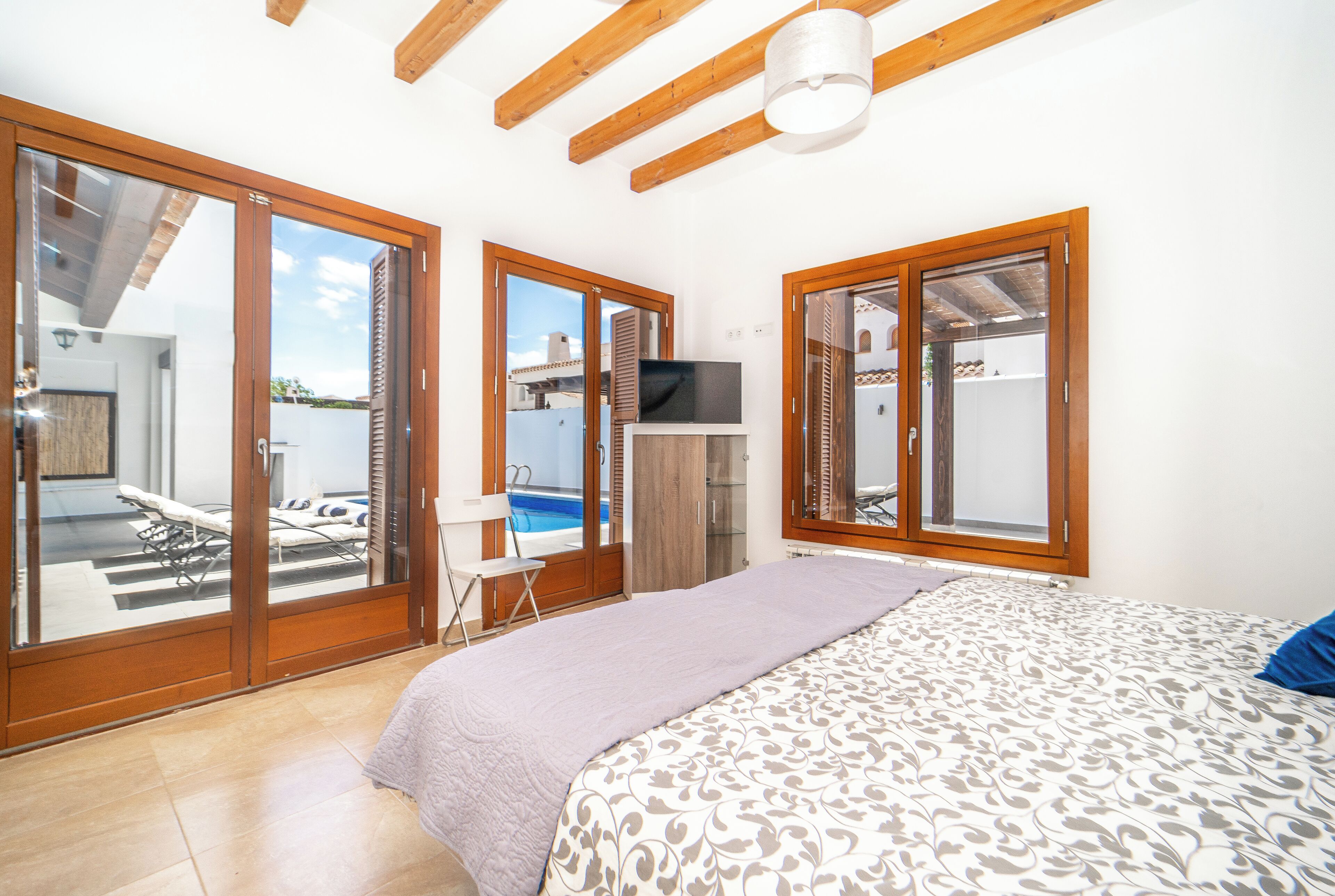A bedroom with a bed, a TV, and a sliding glass door leading to a balcony with a pool.