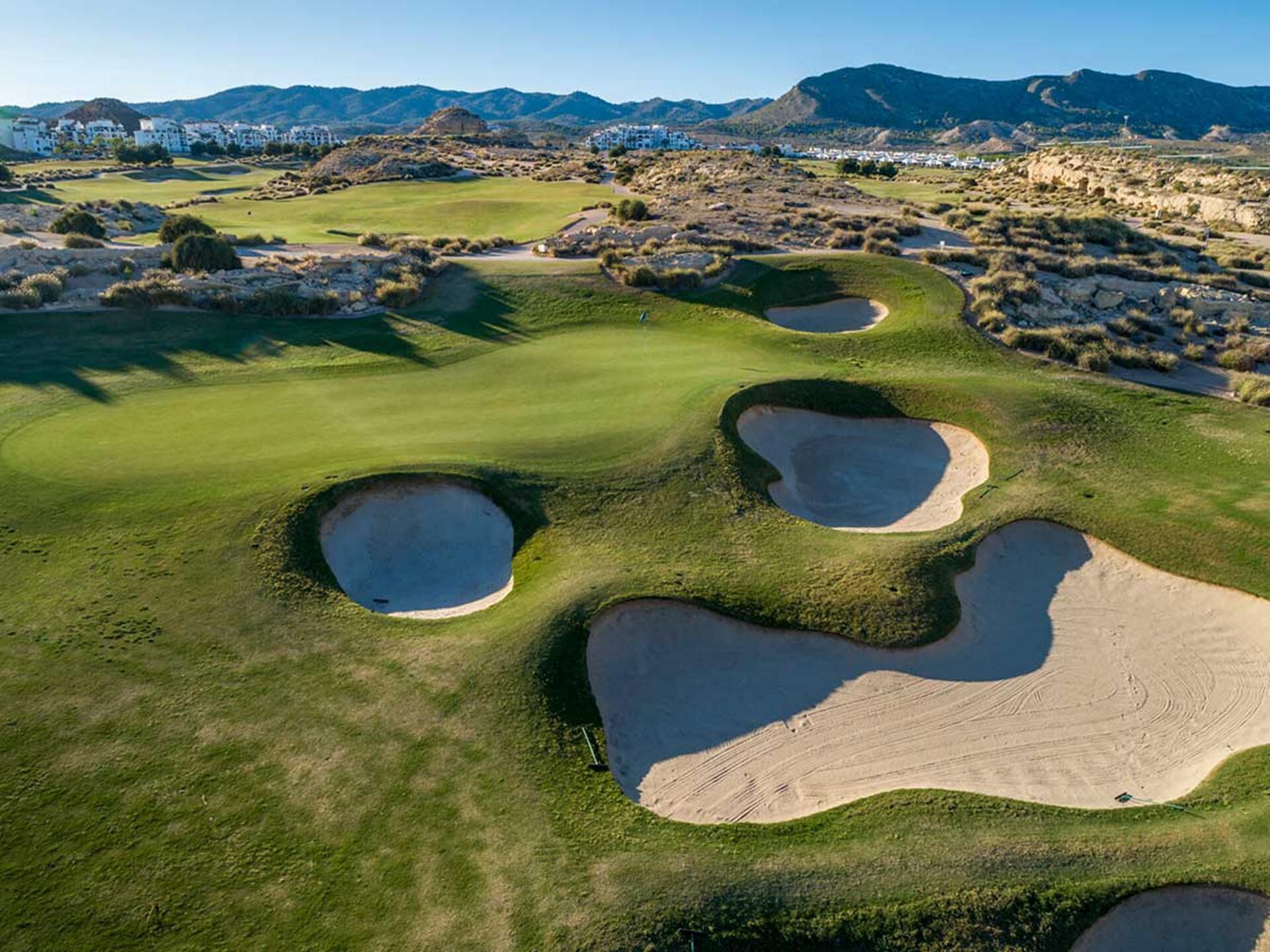 A golf course with bunkers and a mountainous backdrop.