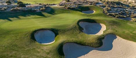 A golf course with bunkers and a mountainous backdrop.